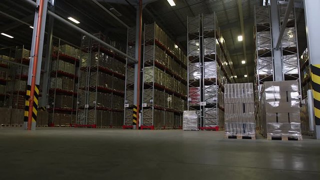 Camera cranes up on shelves of cardboard boxes inside a storage warehouse.
