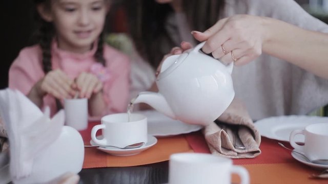 Attractive little girl sharing some secrets with her mother at the cafe. Prety young woman wondering at what her daughter whispering.