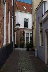 Leiden, The Netherlands - January 20th 2018 - The Schoolsteeg and Lokhorststraat with traditional Dutch houses with old Dutch rooftops with blue sky background and a little empty alley with plants and
