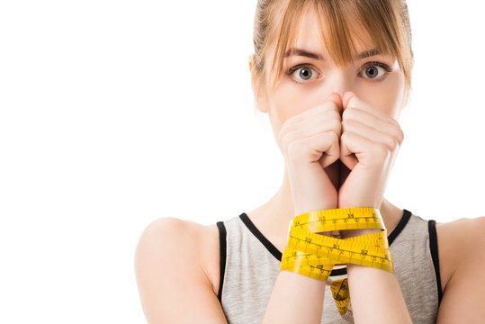 scared young woman covering face with hands tied in measuring tape isolated on white
