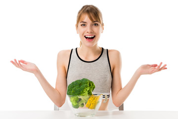 surprised young slim woman with broccoli covered in measuring tape in bowl isolated on white