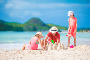 Family making sand castle at tropical white beach. Father and two girls playing with sand on tropical beach