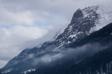 Dramatic mountain scenery with fog shrouding the forest and clouds engulfing the peaks near the Austrian town of Waidring