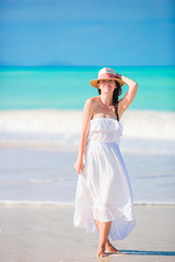 Fototapeta na wymiar Young beautiful woman on white sand tropical beach. Caucasian girl with hat in dress background the sea