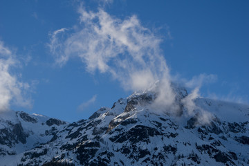 Fototapeta na wymiar Wind swept, snowy mountain peak on a clear blue sky background