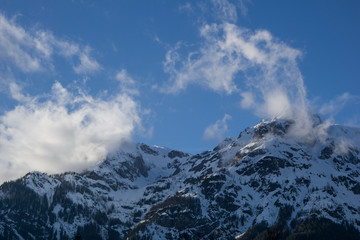 Fototapeta na wymiar Tall, snow covered alpine peaks meeting the clouds on a clear day with blue skies