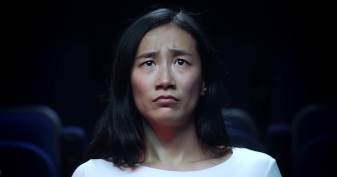 Close up of a frightened, young, Chinese girl at the movie theatre reacting to a horror  movie.