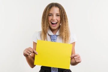 A smiling high school student, blonde with curly hair, holds a blank paper of yellow color, on which can be your promotional information.