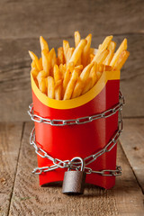 Ban on potatoes for diet and cholesterol reduction. The French fries in the packing box are wrapped around the chain and closed on a padlock. On the background of the old wooden table