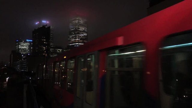 UK December 2017 - A Docklands Light Railway train heads towards Canary Wharf shrouded in low cloud at night in London.