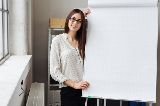 Young smiling woman standing by blank flip chart