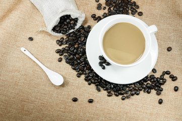 Cup of fresh coffee with coffee beans on burlap warm cup on brown background top view with free space for text