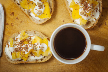 A cup of coffee with pineapple sandwiches, on a black, textured table. Breakfast.