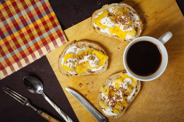 A cup of coffee with pineapple sandwiches, on a black, textured table. Breakfast.