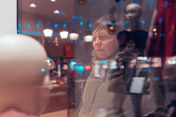 Thoughtful woman looking through shop window at night