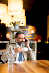 Senior businessman drinking coffee and using mobile phone in lobby