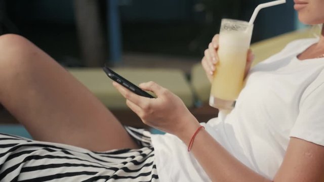 Beautiful and fit young woman with long straight hair with a glass of orange juice on sofa chaise longue by the seaside.