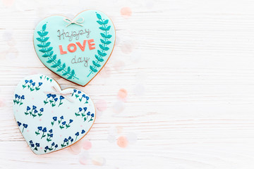 happy valentine's day greeting card. happy love day text on cookie heart and flowers on white rustic wooden background with confetti flat lay. space for text . mock-up