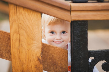 1 year old little caucasian girl palaing hide and seek game outdoors on sunny warm summer day. Closeup portrait of tricky face of blonde baby hiding from parents. Horizontal color photography.