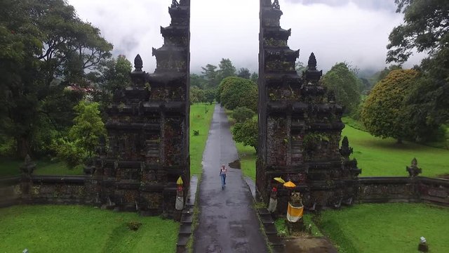 Gliding drone shot of woman hiking through a candi bentar temple gate in Indonesia