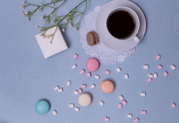 Morning cup of coffee, cake macaron, gift or present box and flower on blue table from above. Beautiful breakfast. Flat lay style.