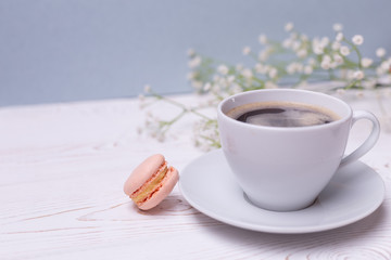 Close-up morning white cup of coffee, cake macaron and flower on blue table. Beautiful breakfast.