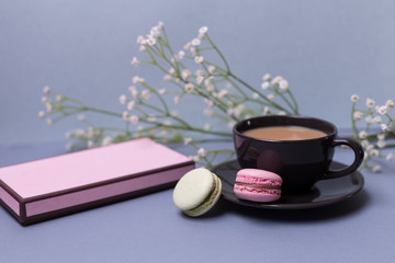Close-up morning black cup of coffee, cake macaron, gift or present box and flower on blue table. Beautiful breakfast.