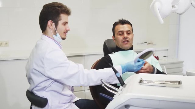 Young professional male dentist working at his clinic giving his mature client a mirror after medical treatment procedure communication medicine trust healthcare practitioner job.
