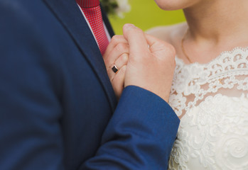 Closeup view of bride and goom holding hands isolated at green nature background. Horizontal color photography.