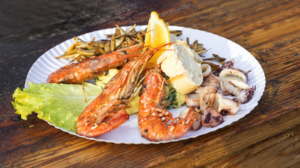 The street food, seafood served on the paper plate. The green letuce, kalamari, shrimps.
