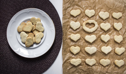 white background dark napkin plate with cookies in the form heart baking paper lies a cookie in shape heart and one place is empty