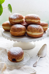 Polish donuts with plum jam on white plateau, plate. Windowsill, white concrete table.