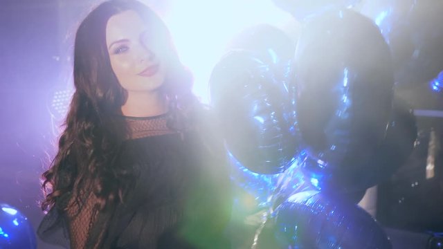 bright balloons into hands of happy brunette with beautiful hair in backlight in fog at evening event