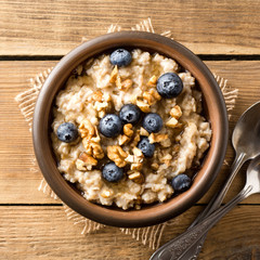 Oatmeal porridge with blueberries, walnuts and honey in ceramic bowl on wooden background.