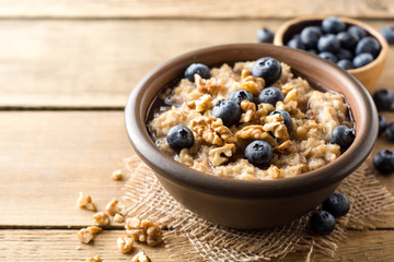 Oatmeal porridge with blueberries, walnuts and honey in ceramic bowl on wooden background.