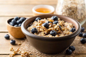 Oatmeal porridge with blueberries, walnuts and honey in ceramic bowl on wooden background.