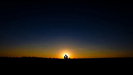 Naklejka na ściany i meble Silhouette of a loving couple over sunset background. a guy and a girl hug and kiss on the horizon in front of the sun