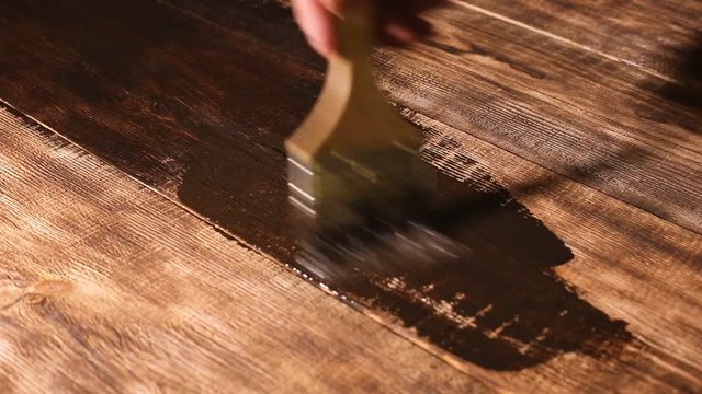 male hand paint wooden surface with brown paint using a paintbrush