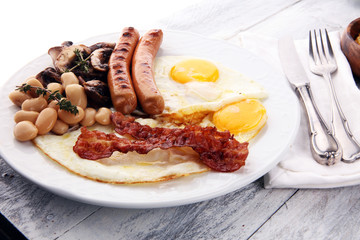 Traditional full English breakfast with fried eggs, sausages, beans, mushroomsand bacon on wooden background