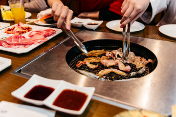 Tourists grilling sliced pork in charcoal grille with tong at the restaurant in Sapporo, Hokkaido, Japan.