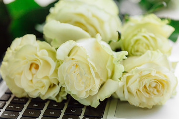 Bouquet of white roses lying on laptop. Top view