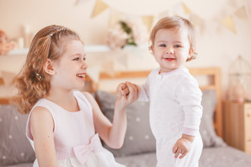 Two cute adorable white Caucasian girsl sisters smiling laughing. Children sitting together on bed in bedroom playing. Lifestyle real true emotions, sibling love