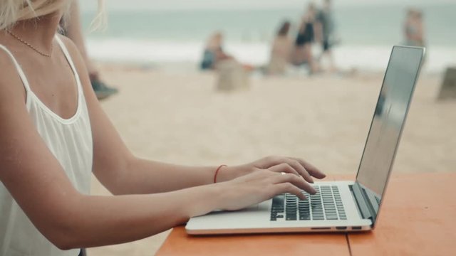 Beautiful girl with a laptop working in beach cafe woman freelancer close up