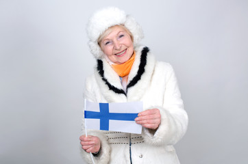 Senior woman holding a flag of Finland. Adult woman is 70 years of age. Pensioner. Old female is dressed in warm winter clothes standing on a light background.