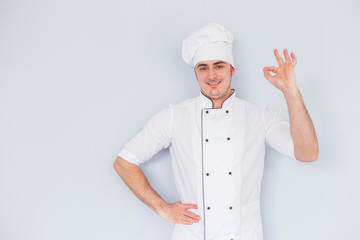 Young chef cook shows ok on a white background.