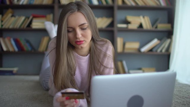 Beautiful teenage girl shopping online with credit card and tablet at home. 4 k Pretty young teenage girl shopping online using her credit card and laptop computer