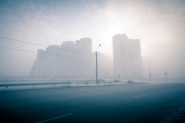 Urban landscape. Foggy winter cityscape. Foggy city street with silhouettes of residential buildings.