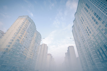 Looking up at modern city street. Foggy winter cityscape. Foggy city street with silhouettes of high residential buildings.