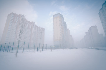 Foggy winter cityscape. Foggy city street with silhouettes of high residential buildings.