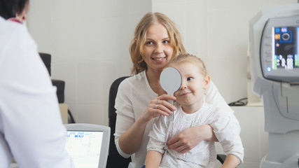 Optometrist checks child's eyesight - mother and child in ophthalmologist room